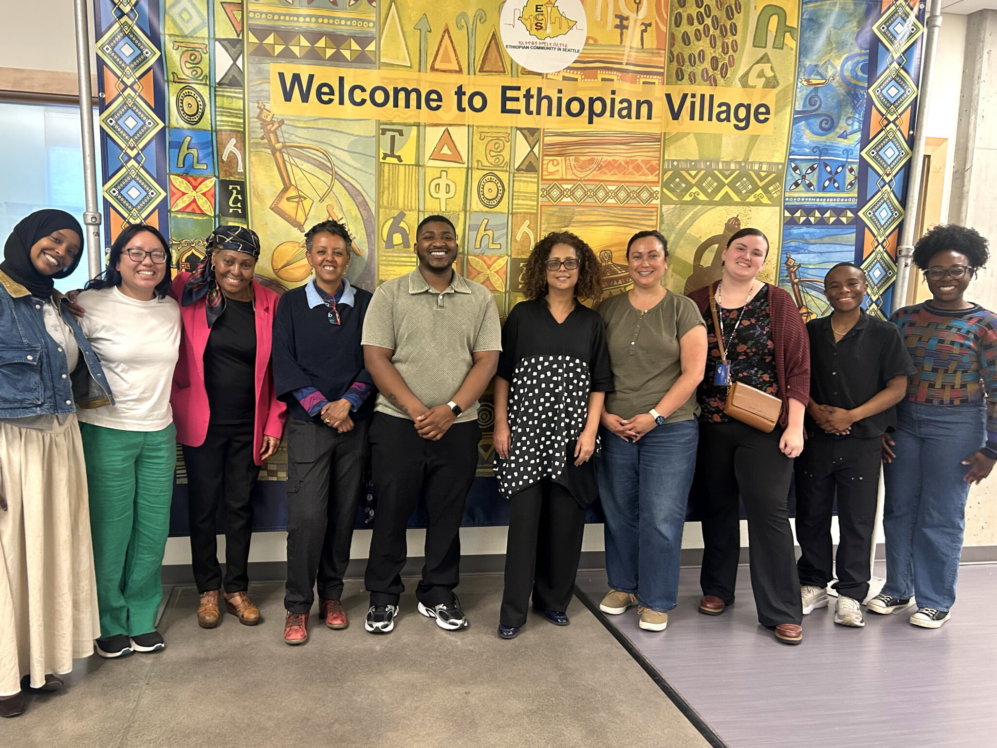 A group photo inside Ethiopian Village. In the background is a large tapestry that says "Welcome to Ethiopian Village".