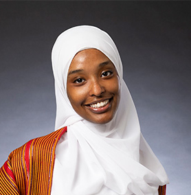 Headshot of a person wearing a head covering, against a black and white gradient background.